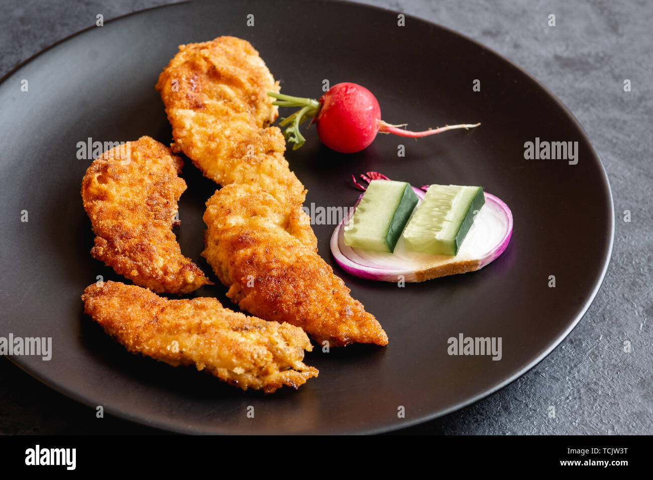 Fried chicken sirloin in breadcrumbs on a black dish. Stock Photo