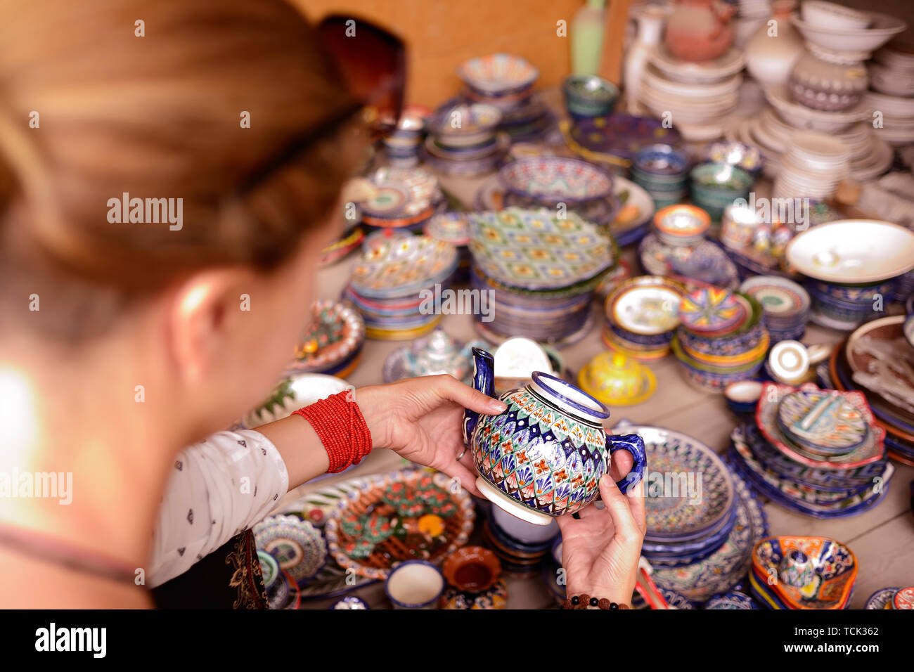 Watching tourist handmade colourful ceramic pottery with jug and cups selling at street stall in Rishton, Uzbekistan Stock Photo