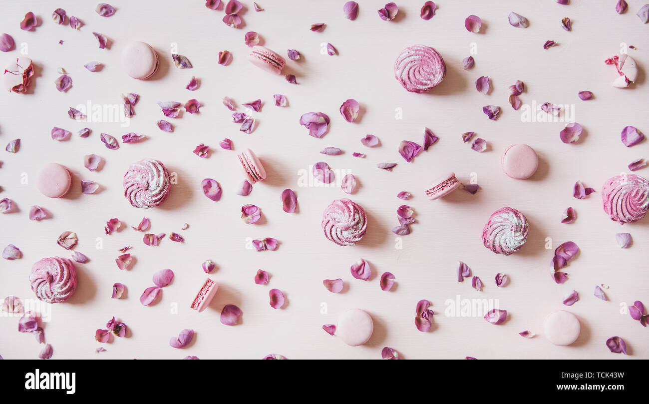 Flat-lay of macaron cookies, marshmallows and petals over pink background Stock Photo