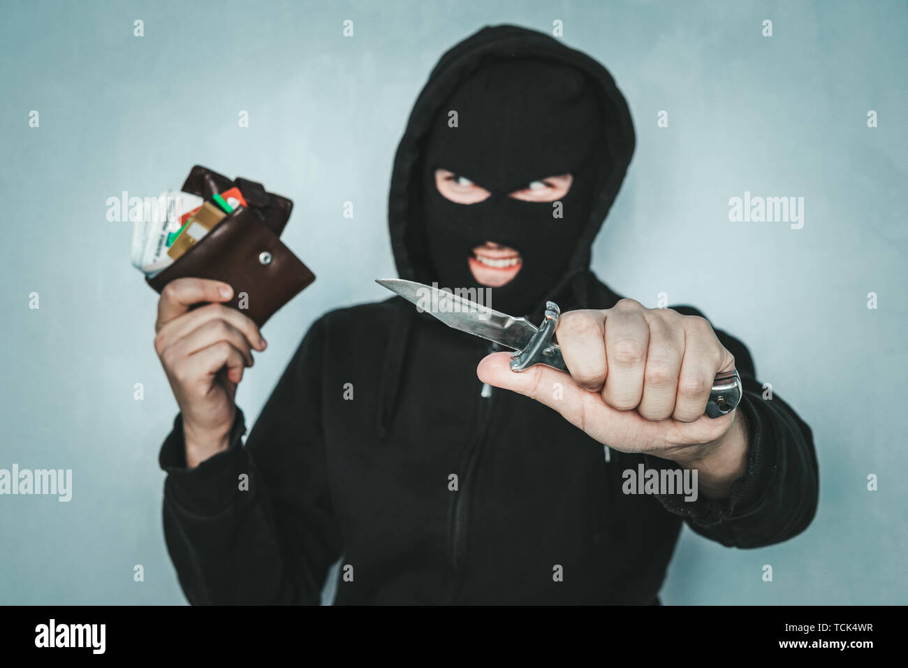 criminal robbery concept. An evil robber threatens with a knife and holds a stolen purse in his hand. Mortal danger. The malevolent thief smiles. Stock Photo