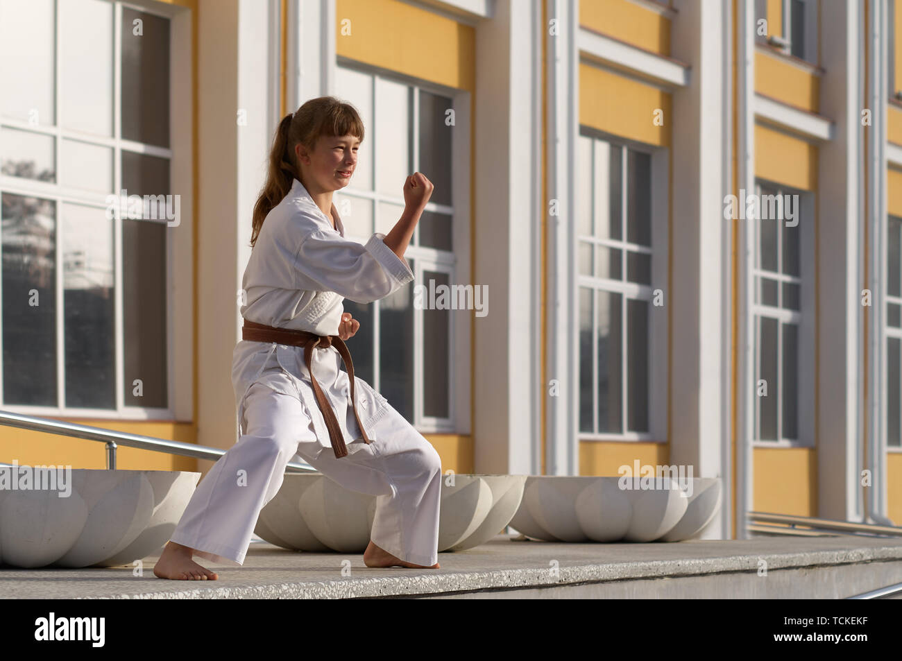 Young Woman in Kimono doing formal karate exercising on cityscape background Stock Photo