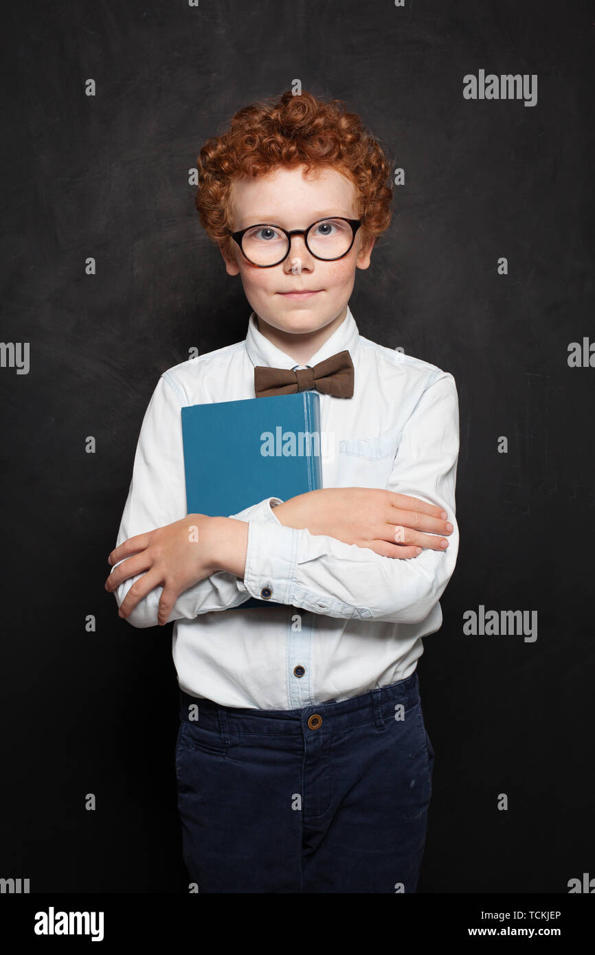 Cute little boy holding book. Ginger haired kid on chalkboard background Stock Photo