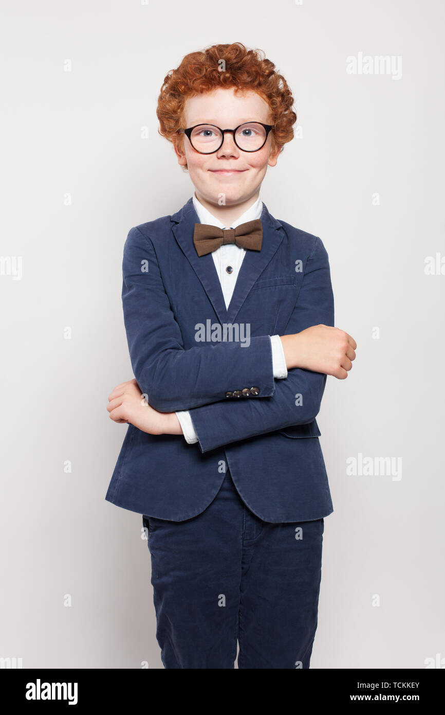 Happy red haired child boy in blue suit standing against white wall background Stock Photo