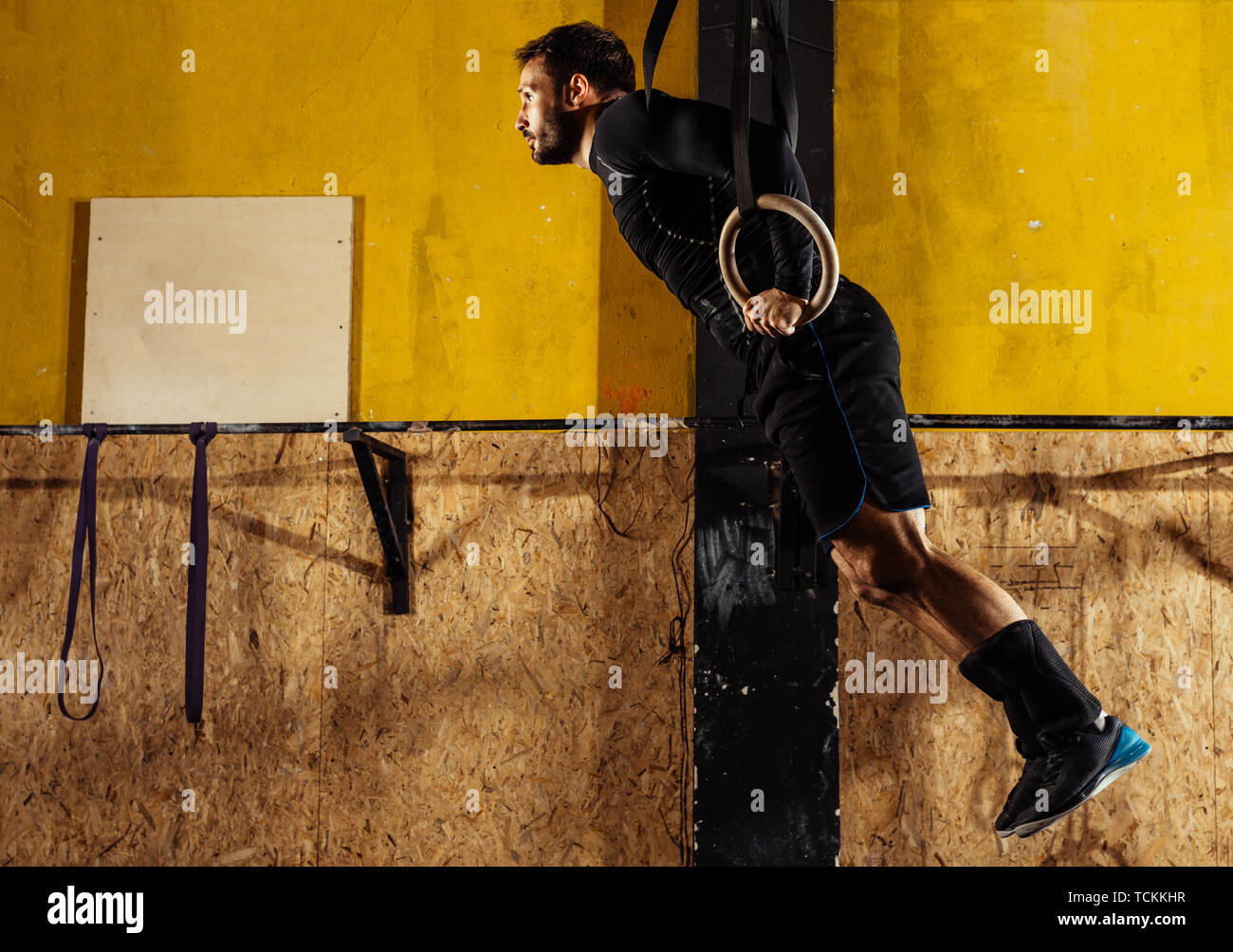 Strong young man doing pullups exercise using gymnastic rings at gym