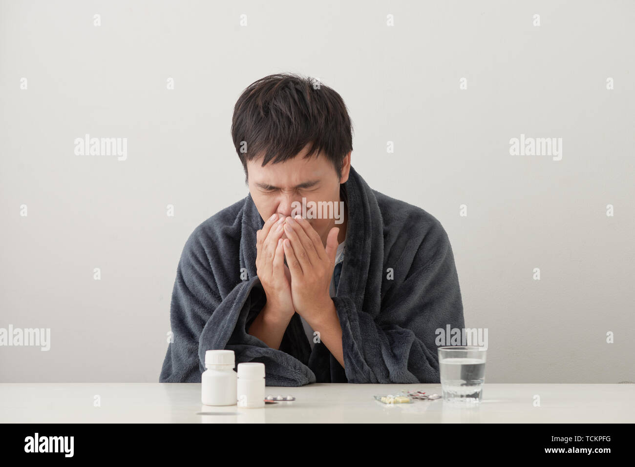 young sick and ill man in sofa holding tissue cleaning snotty nose having temperature feeling bad infected by winter grippe virus in flu and influenza Stock Photo