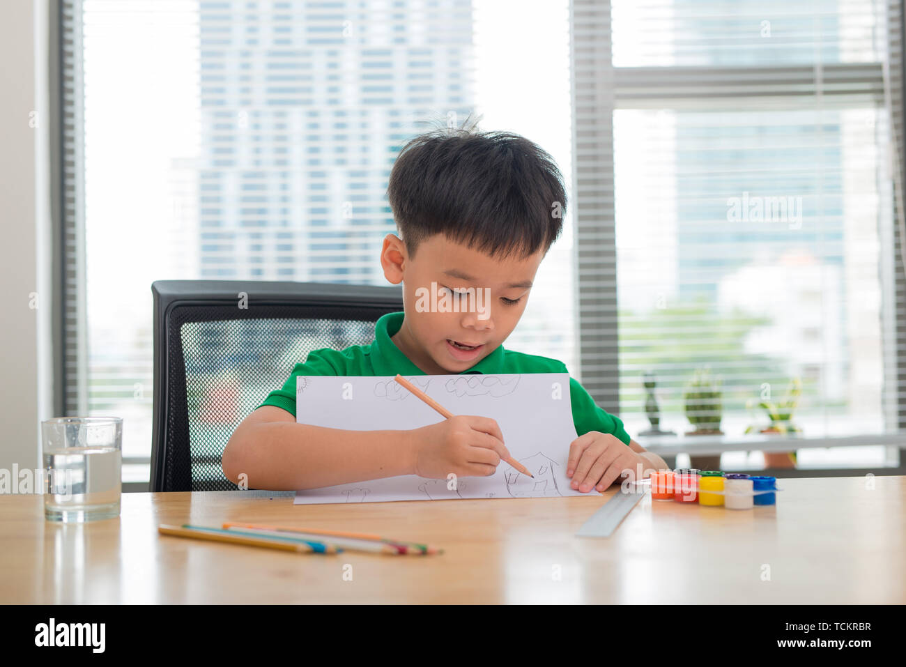 Cute confused smiling boy doing homework, coloring pages, writing and painting . Children paint. Kids draw. Preschooler with books in the library. Col Stock Photo