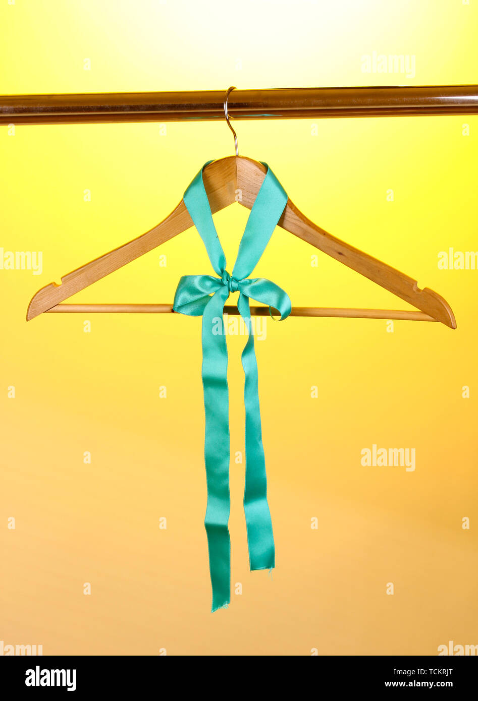 Beautiful turquoise bow hanging on wooden hanger on yellow background Stock Photo