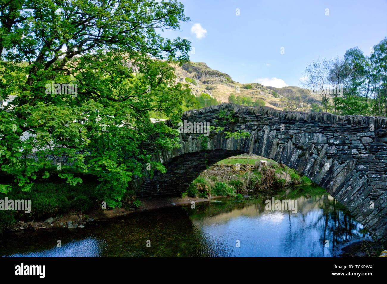 Stone built arch bridge over stream in Langdale in English Lake District in evening sunshine with large boulder in foreground Stock Photo