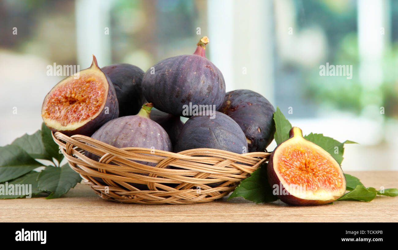 Ripe sweet figs with leaves in basket, on wooden table, on window