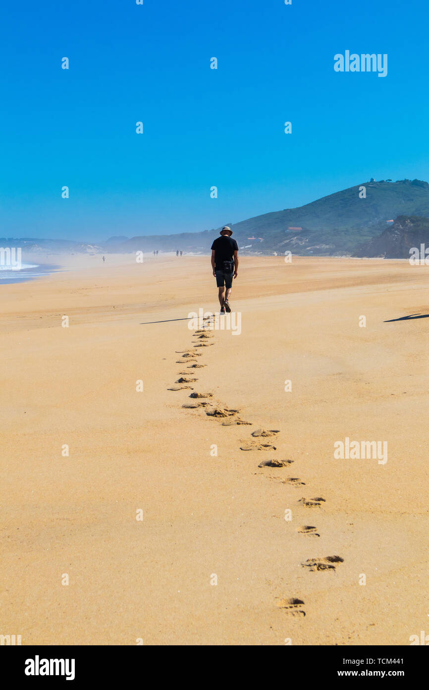 Lone man walking along beach leaving a trail of footprints in the sand Stock Photo
