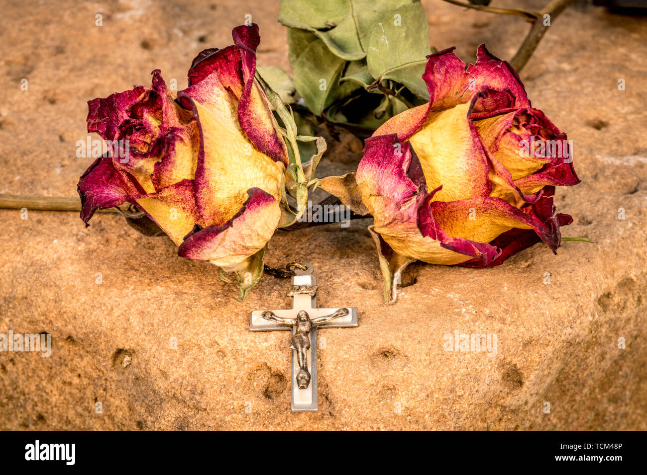 Christian cross on rosary and a dry yellow red roses lie on a red ...