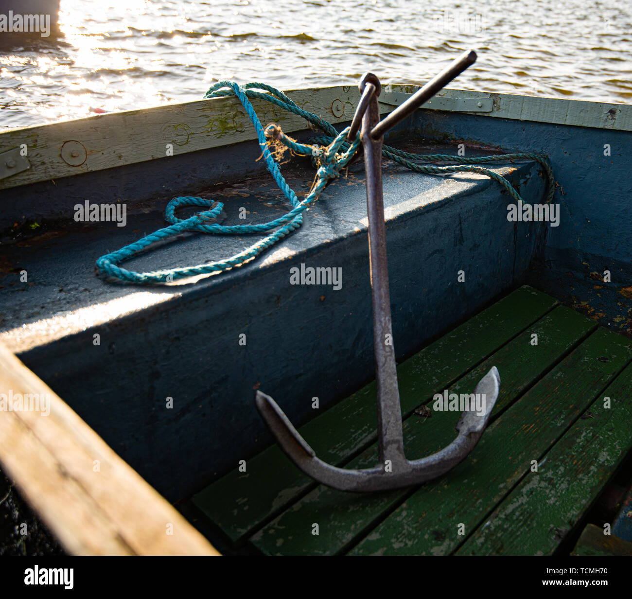 A large metal anchor sits inside a small blue rowing boat. Taken during an early sunset on a small lake Stock Photo