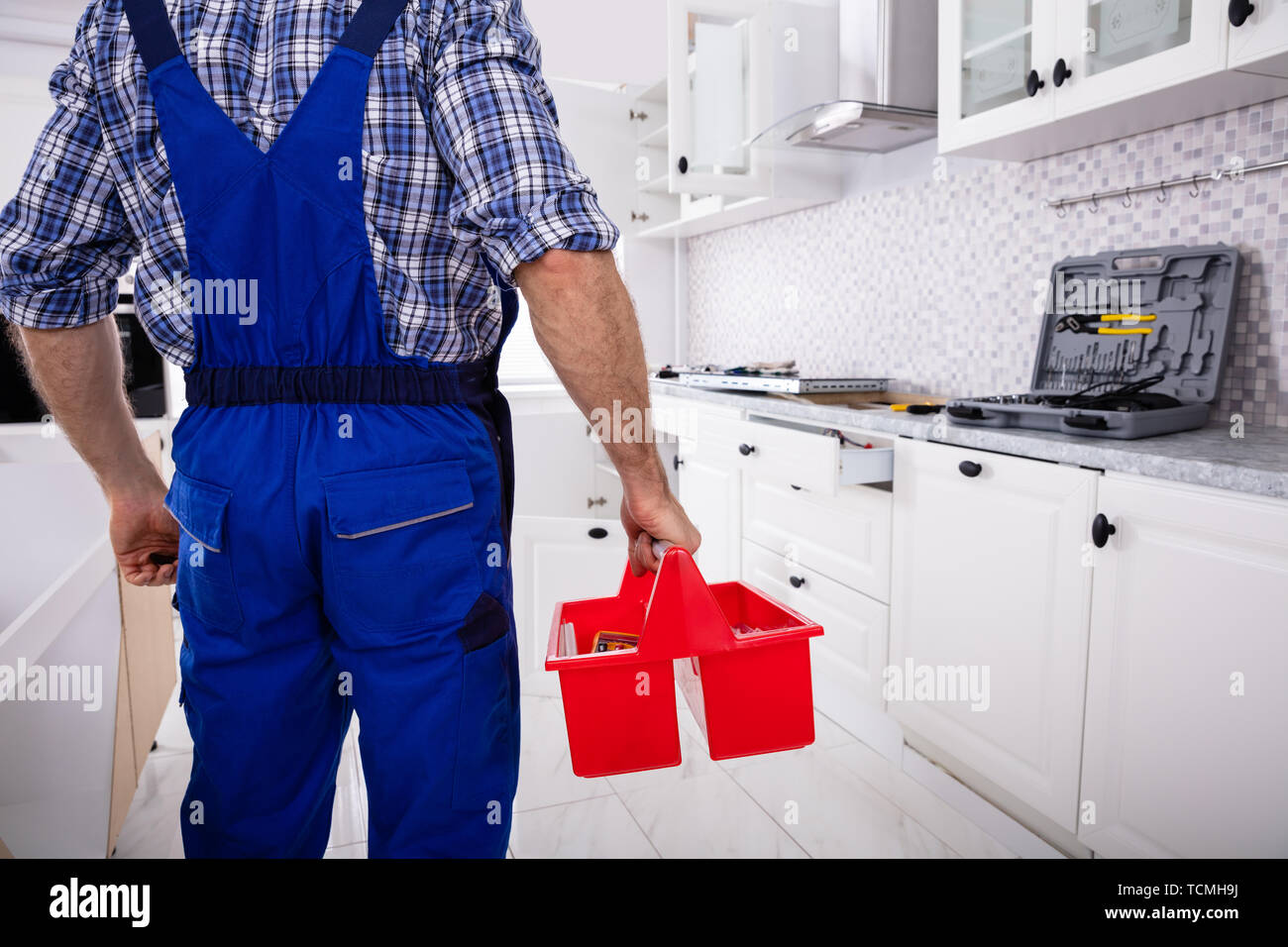 Rear View Of A Repairman In Uniform Holding Tool Box Installing Kitchen Induction Ceramic Hob Stock Photo