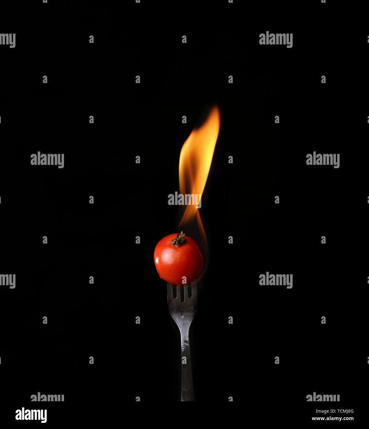 Tomato on fire with blue flames isolated on black background Stock
