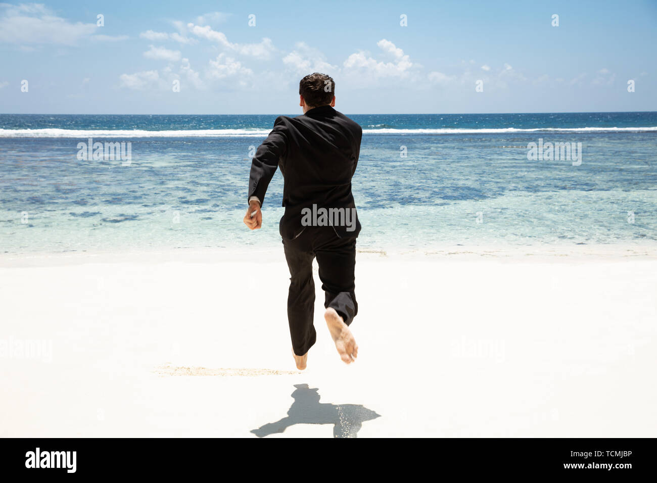 Rear View Of A Businessman Running Barefoot Toward The Idyllic Sea At Beach Stock Photo