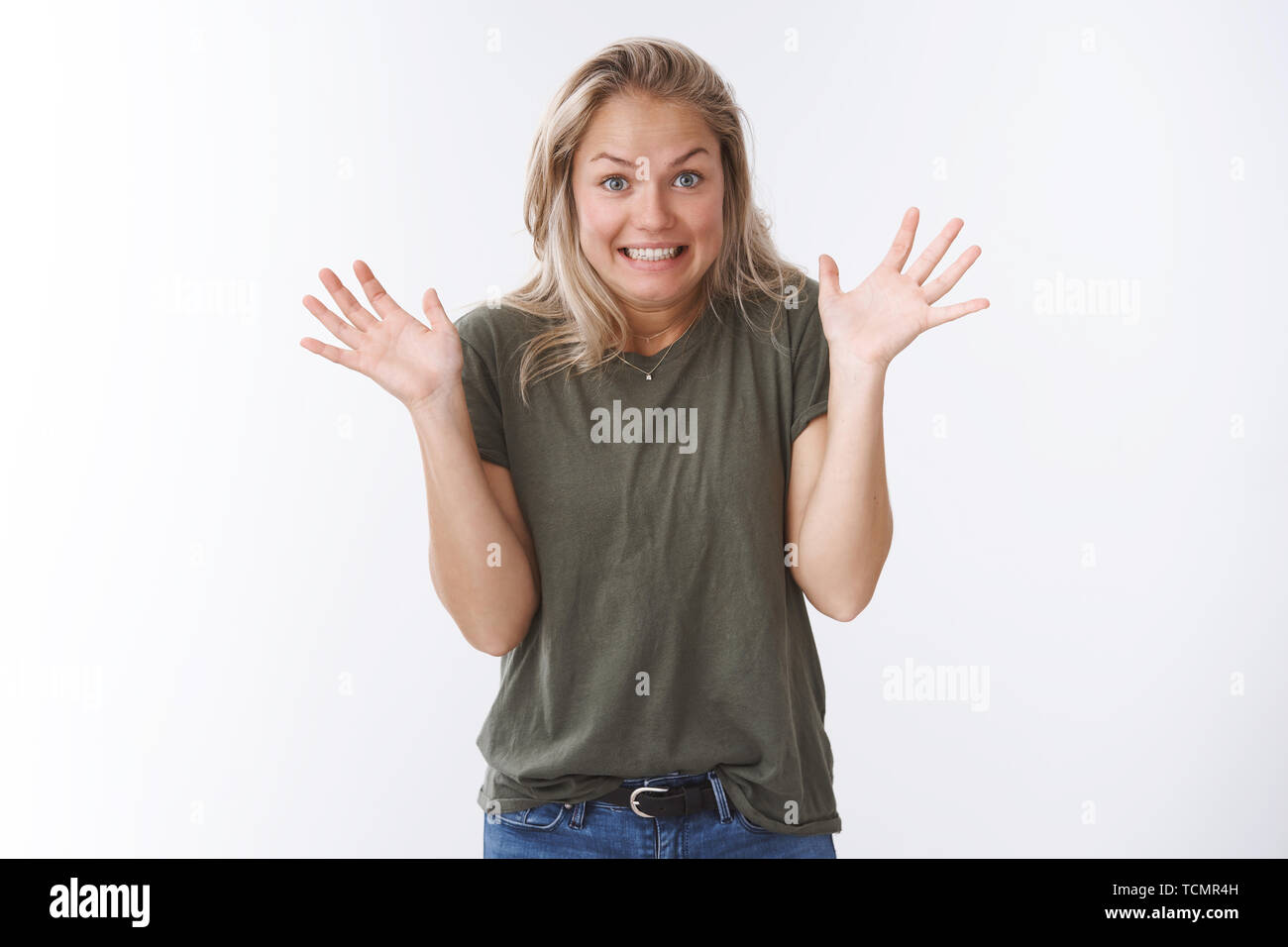 Yikes sorry. Studio shot of awkward cute blond woman raising palms in apology gesture smiling excusing for not making mistake on purpose posing guilty Stock Photo