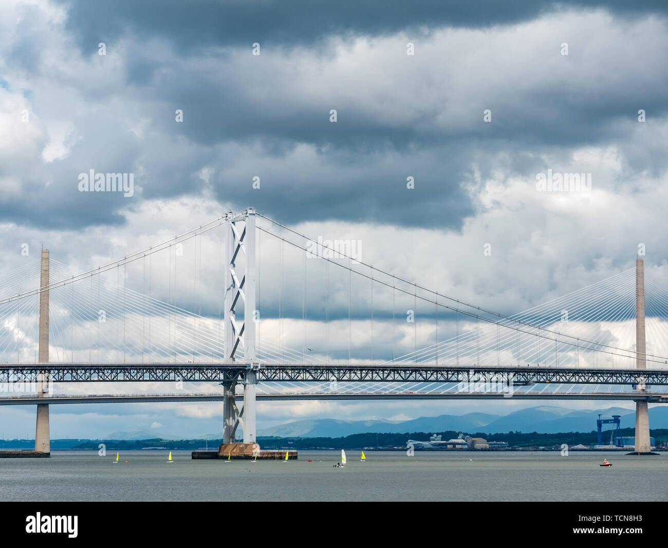 South Queensferry, Scotland, United Kingdom, 9th June 2019 UK Weather: Dramatic light and dark clouds gather over the Forth Road Bridge and the Queensferry Crossing with bright yellow sailing dinghies creating a stark colour and size contrast in the Forth river Stock Photo
