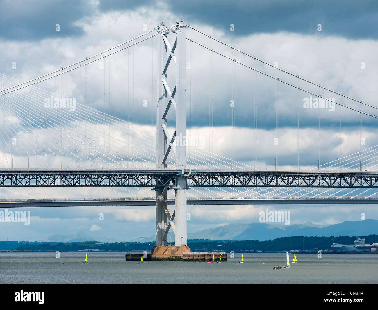 South Queensferry, Scotland, United Kingdom, 9th June 2019 UK Weather: Dramatic light and dark clouds gather over the Forth Road Bridge and the Queensferry Crossing with bright yellow sailing dinghies creating a stark colour and size contrast in the Forth river Stock Photo