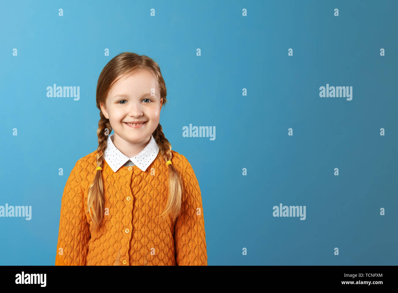 Closeup portrait of a little girl schoolgirl. Pretty child in a yellow sweater on a blue background. Copy space Stock Photo