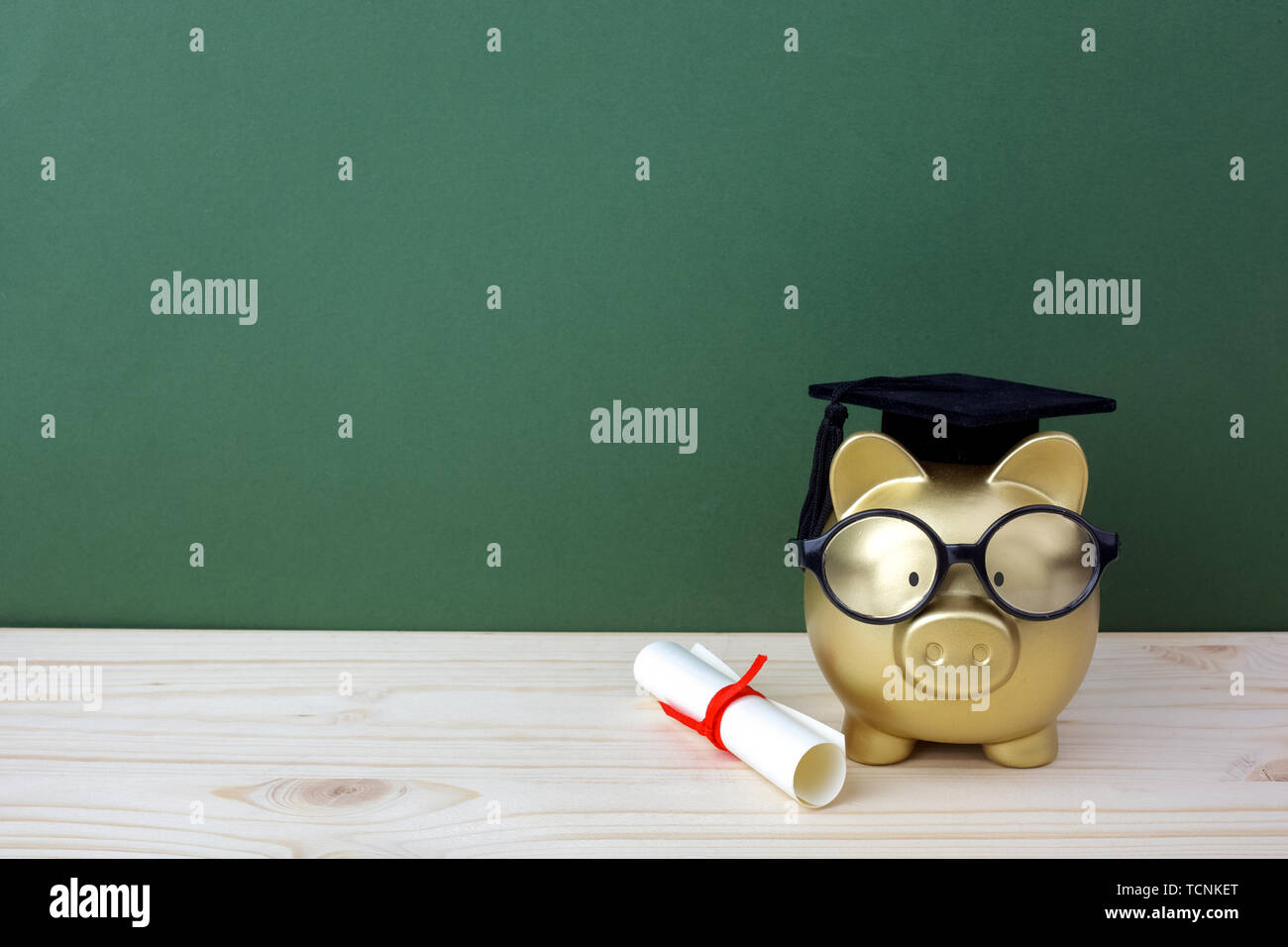 Gfold piggy bank with a grad cap and diploma in front of green ...