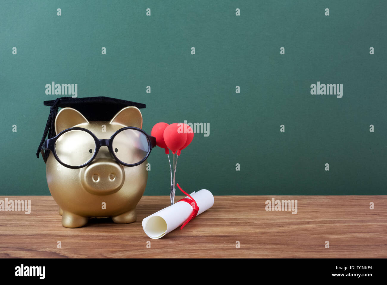Gfold piggy bank with a grad cap and diploma in front of green ...