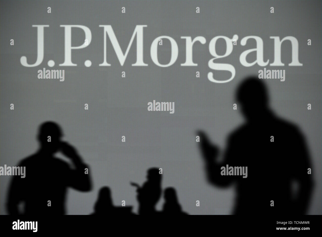 The JP Morgan logo is seen on an LED screen in the background while a silhouetted person uses a smartphone in the foreground (Editorial use only) Stock Photo