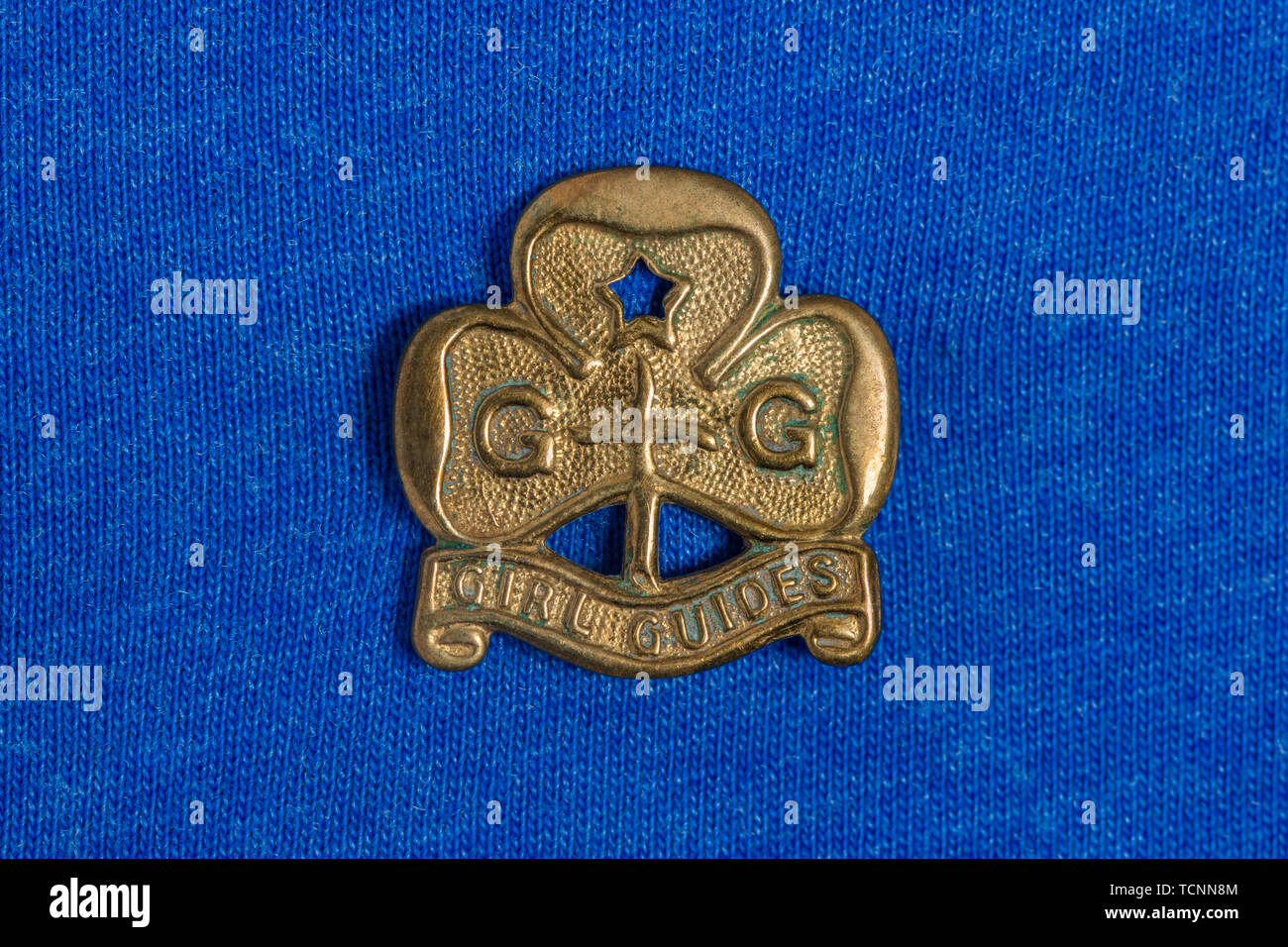 A vintage brass Girl Guides badge shot on a blue cotton background. Stock Photo