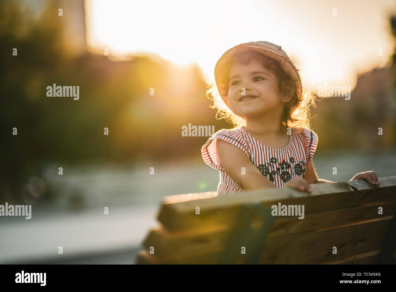 Portrait of a cute beautiful and happy girl standing on bench in the park. Stock Photo