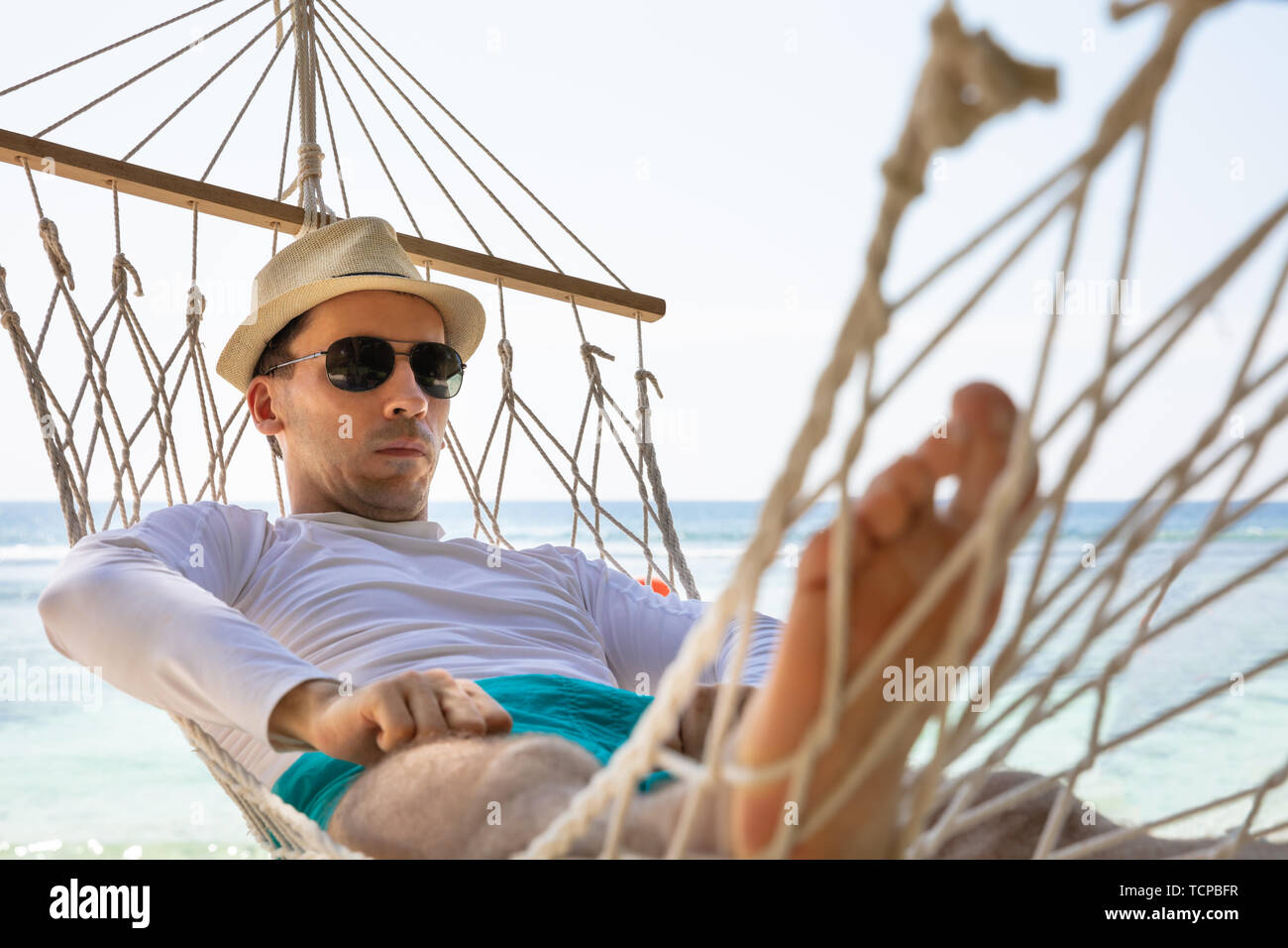 Close-up Of A Man Wearing Sunglasses Lying On Hammock In Front Of Sea At Beach Stock Photo