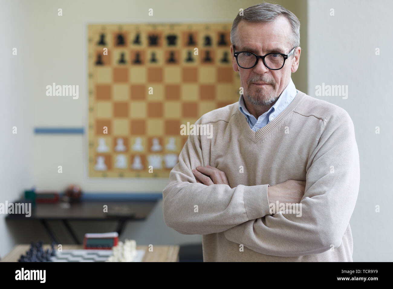 Aged male principal of chess club posing for pictures for advertising chess classes for schoolchildren Stock Photo