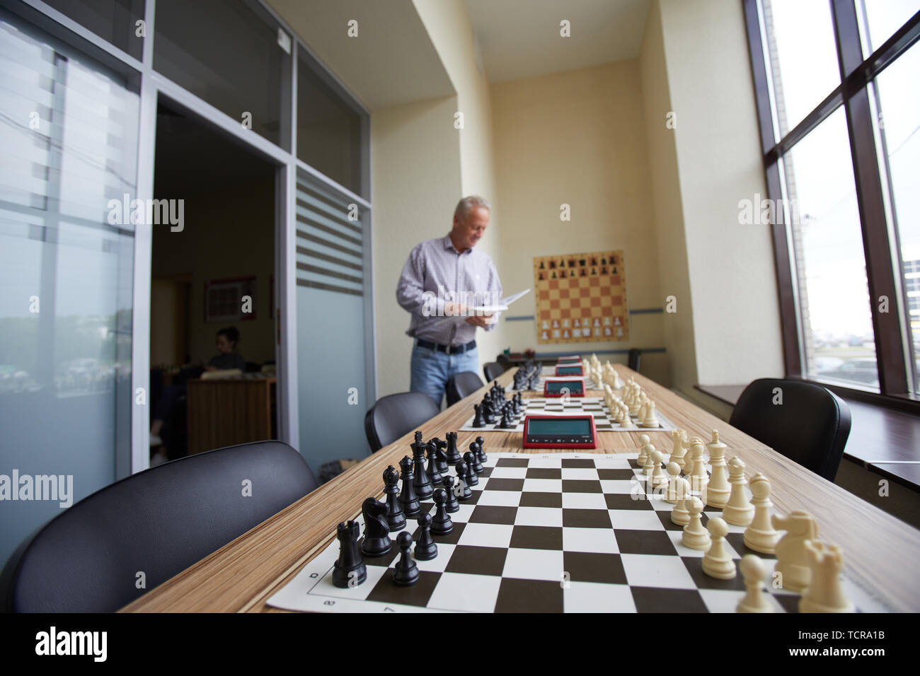 Aged male teacher in shirt checking how well prepared classroom is before next chess class Stock Photo