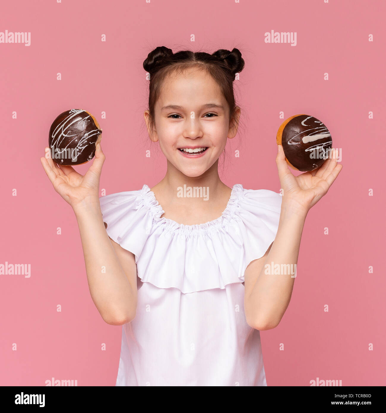 Happy little girl holding chocolate covered donuts and smiling Stock Photo