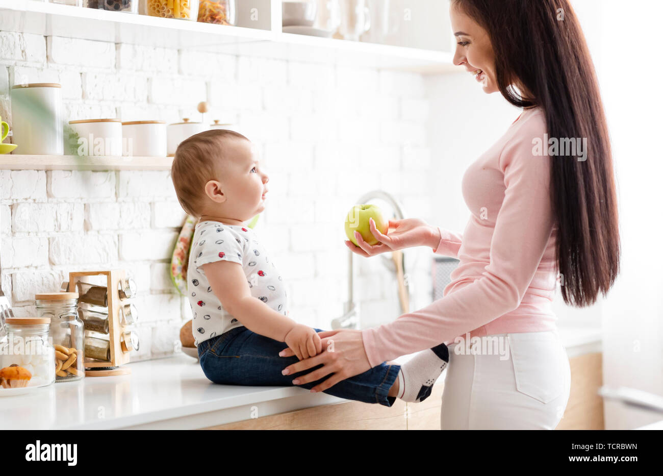 Lovely mother offering fresh green apple to her cute baby Stock Photo