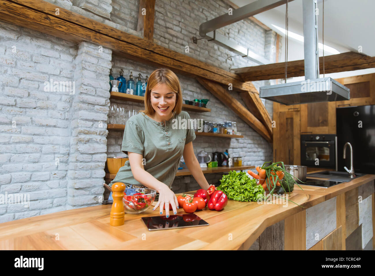 Young woman preparing food in the rustic kitchen while using digital tablet Stock Photo