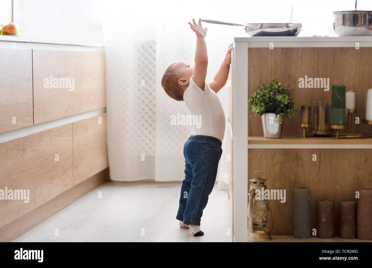 child safety at home concept - toddler reaching for pan on the stove in kitchen Stock Photo