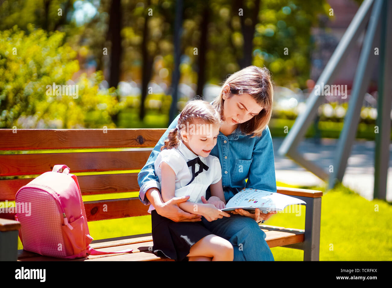 Mother and little daughter in outdoors public park sitting on the bench ...