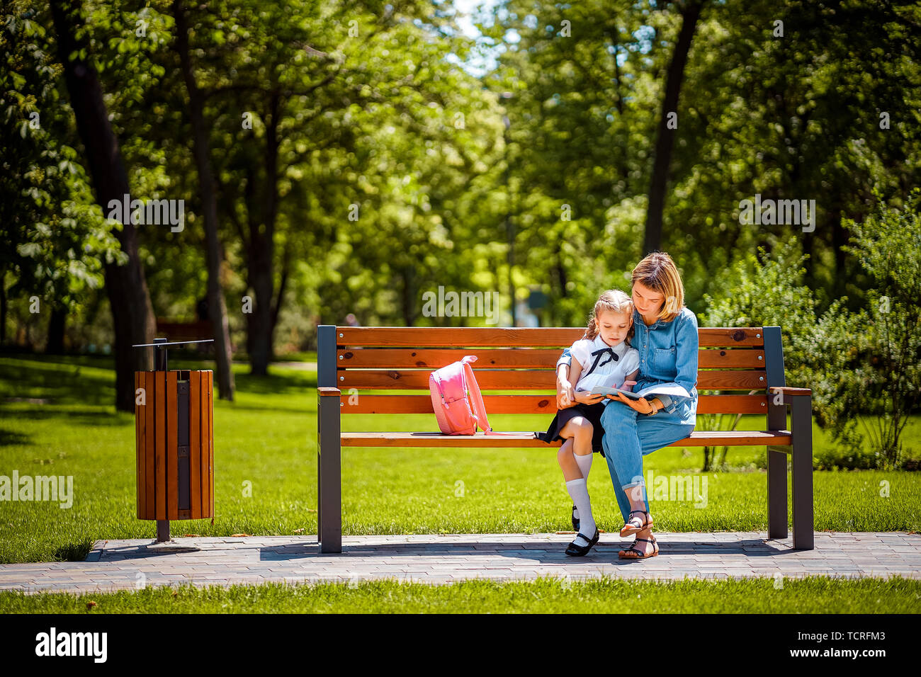 Mother and little daughter in outdoors public park sitting on the bench ...