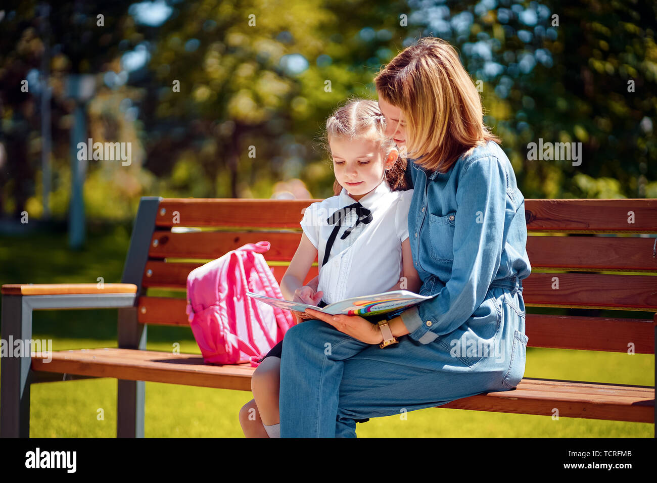 Mother and little daughter in outdoors public park sitting on the bench ...