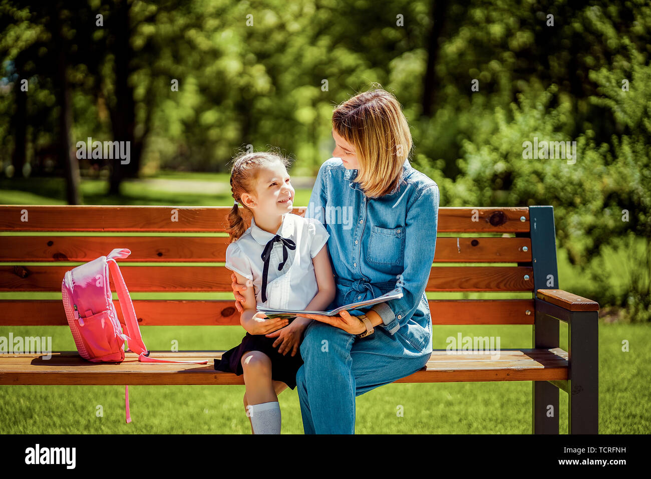Mother and little daughter in public park sitting on the bench and look ...