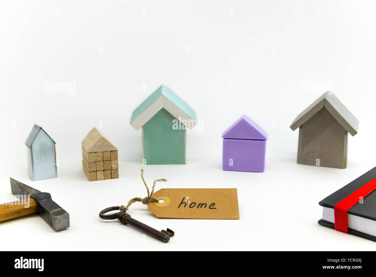 Five small houses made of different materials. Key with shield, hammer and book in the foreground. Stock Photo