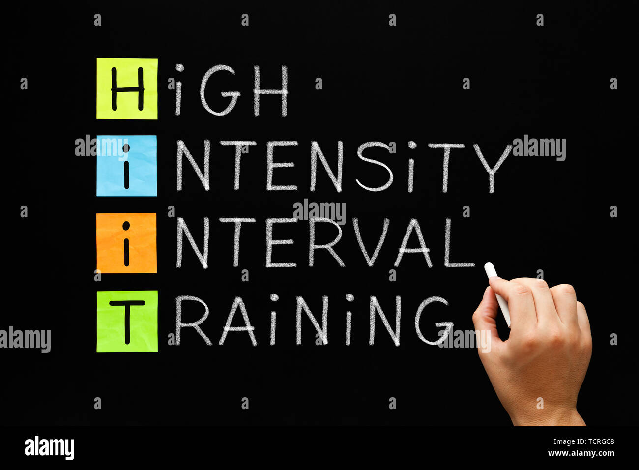 Hand writing fitness workout acronym HIIT - High Intensity Interval Training with white chalk on blackboard. Stock Photo