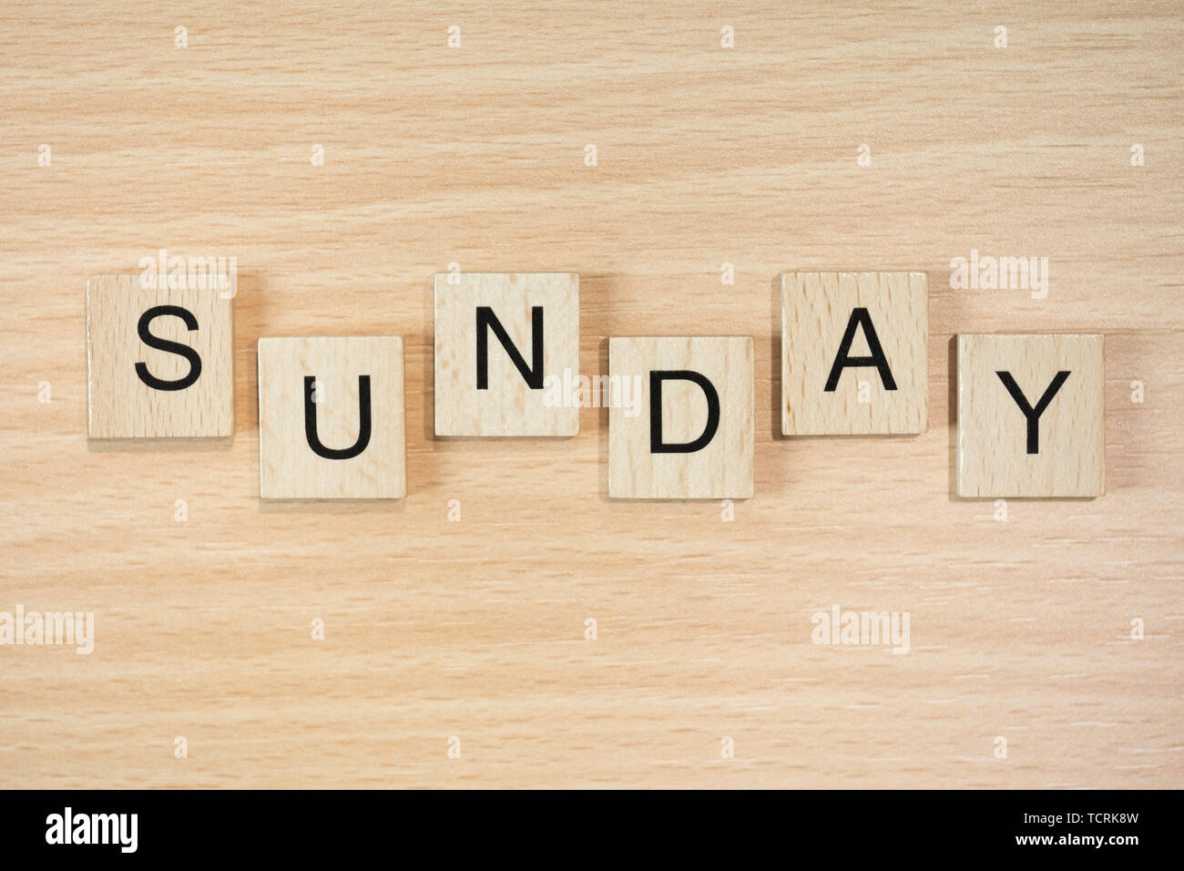 The word Sunday, spelt out using wooden tiles on a wood effect background. Stock Photo