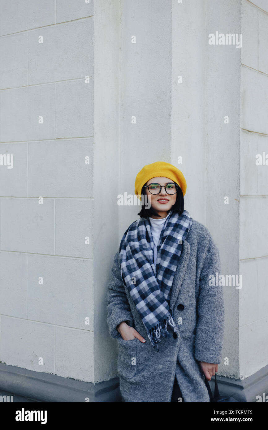 Attractive young girl in stylish glasses in coat and yellow Beret on a simple light background Stock Photo