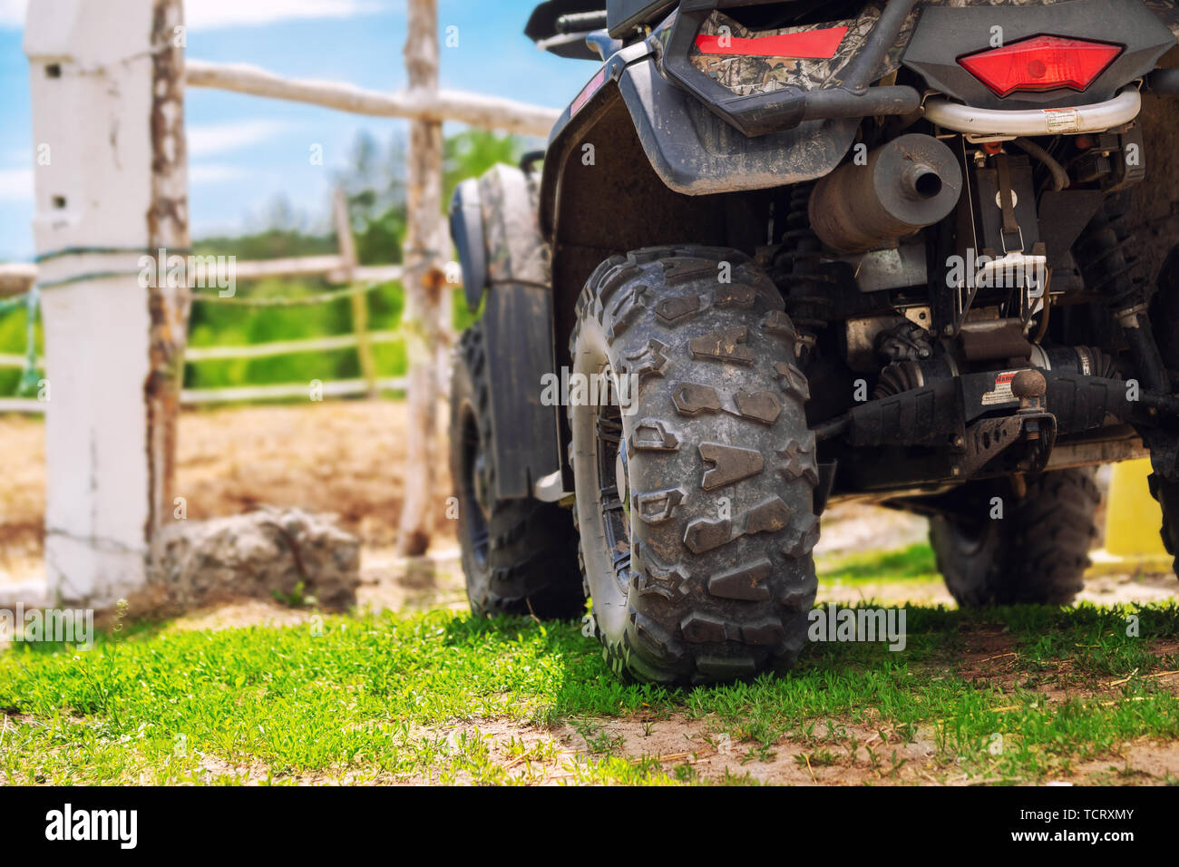 ATV quad bike vehicle standing near wooden fence at farm or horse stable. Back view of all wheel drive motorcycle at farm. Rural countryside machine Stock Photo