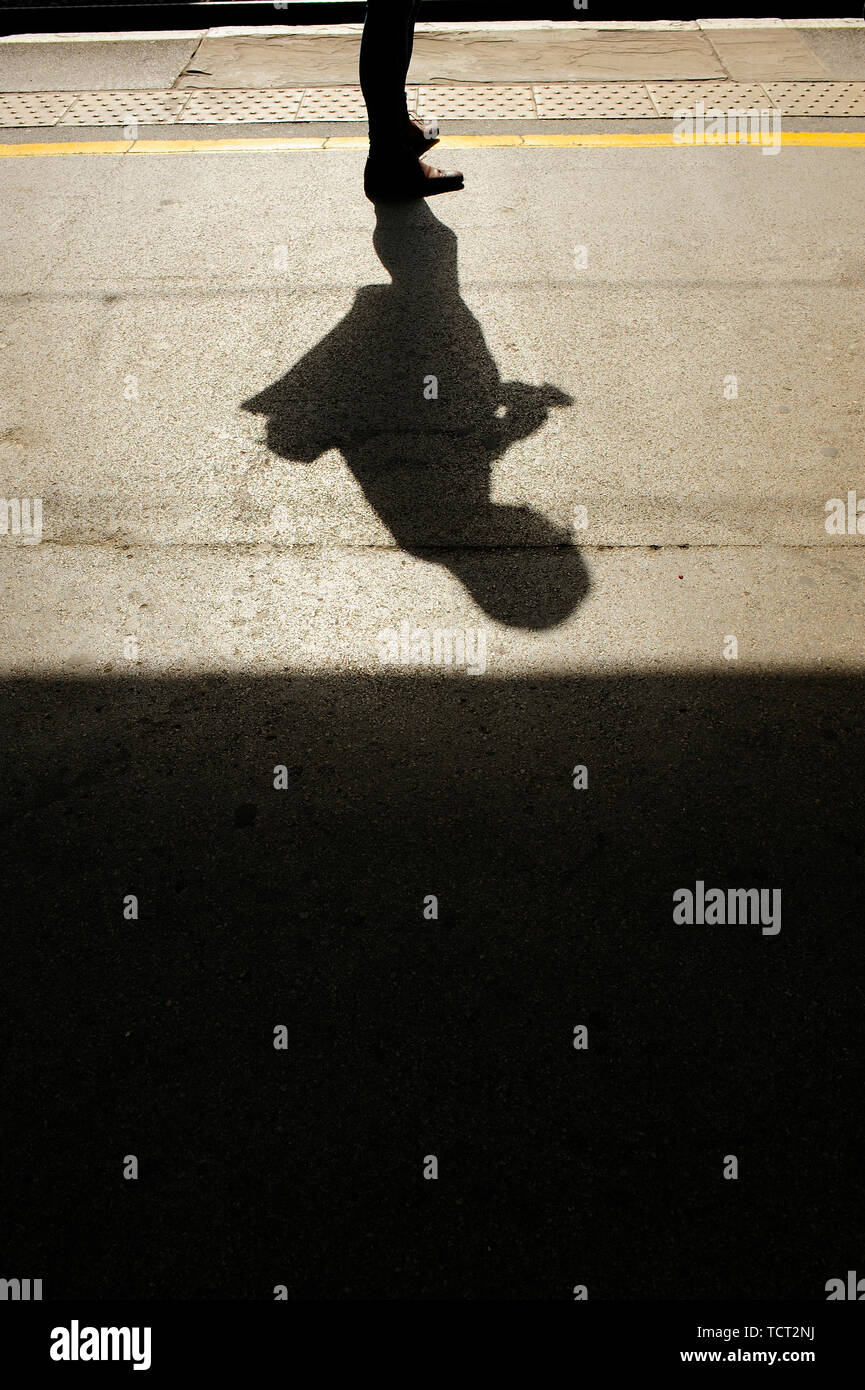 Shadow and silhouette of young man stood on railway station platform using a mobile phone Stock Photo