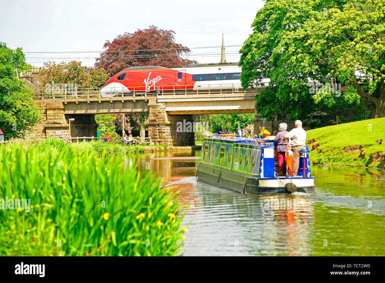 Virgin inter city train speeding over a bridge on the Lancaster Canal with slow moving narrow boat passing underneath at Lancaster on a sunny day Stock Photo
