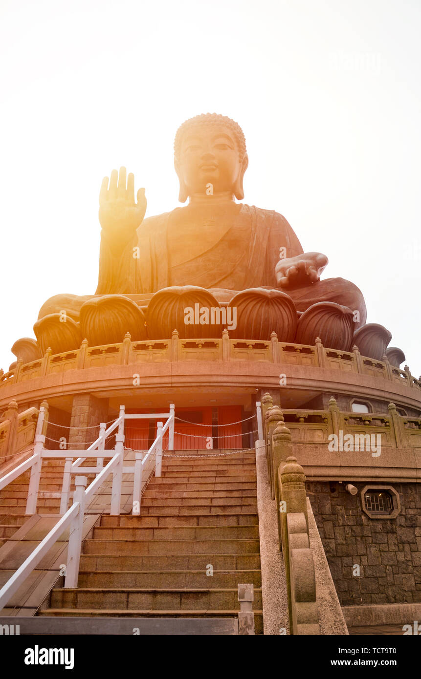 The enormous Tian Tan Buddha at Po Lin Monastery in Lantau Island, Hong Kong. Photographed during sunset with orange sun shining behind the statue. Popular tourist attraction. Stock Photo