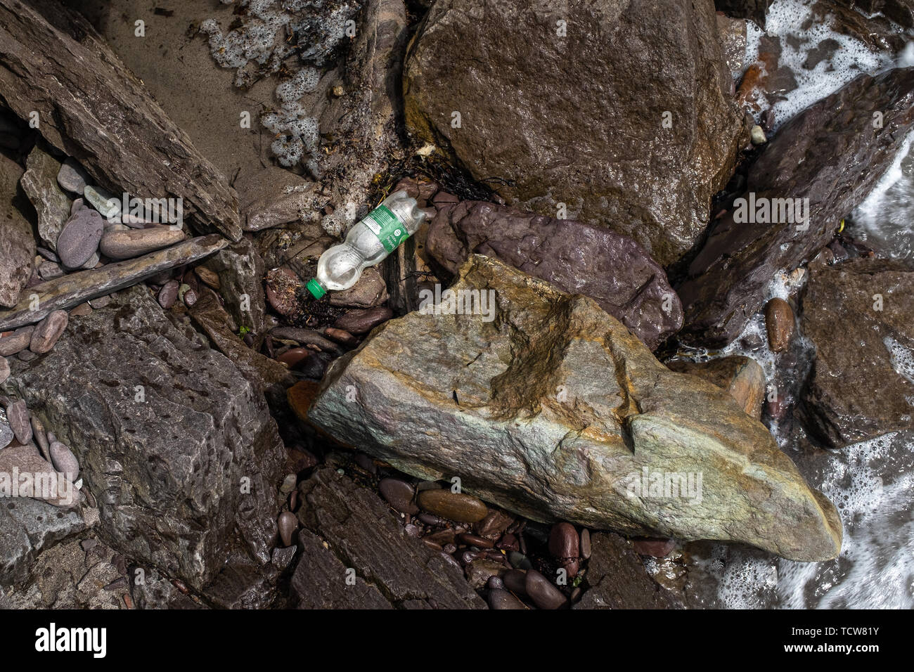 A single plastic bottle is washed up between rocks on the coastline of Ireland, nobody in the image Stock Photo