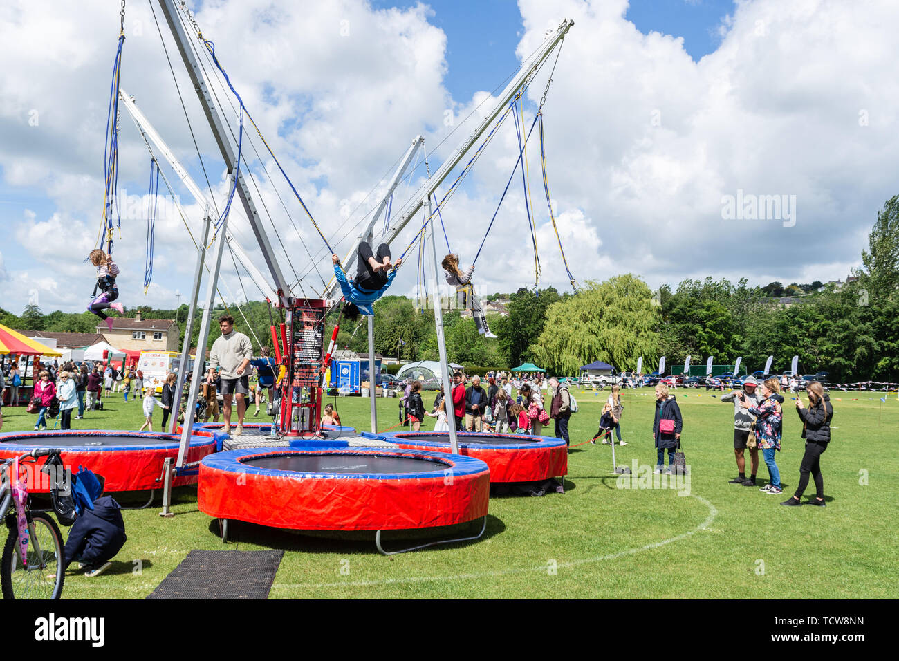Children bouncing and somersaulting on a bungee trampoline while adults watch at the annual Bradford on Avon Lions funday Stock Photo