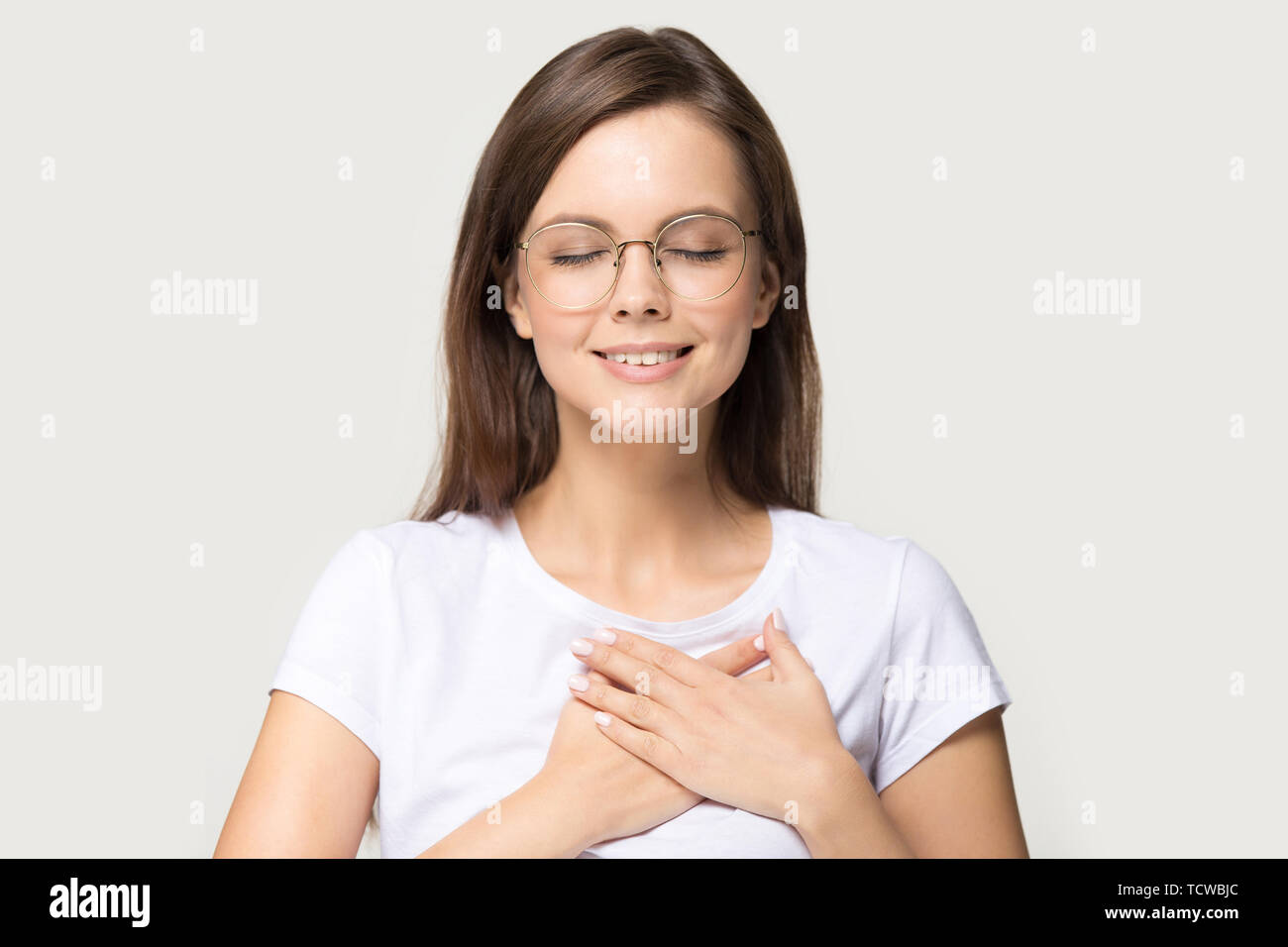 Headshot portrait gratitude woman closed eyes holding hands on chest Stock Photo